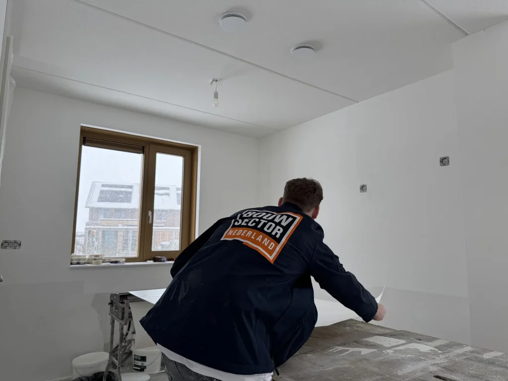 Vakman van Bouwsector Nederland tilt een ingelijmde baan vlies van de werktafel
