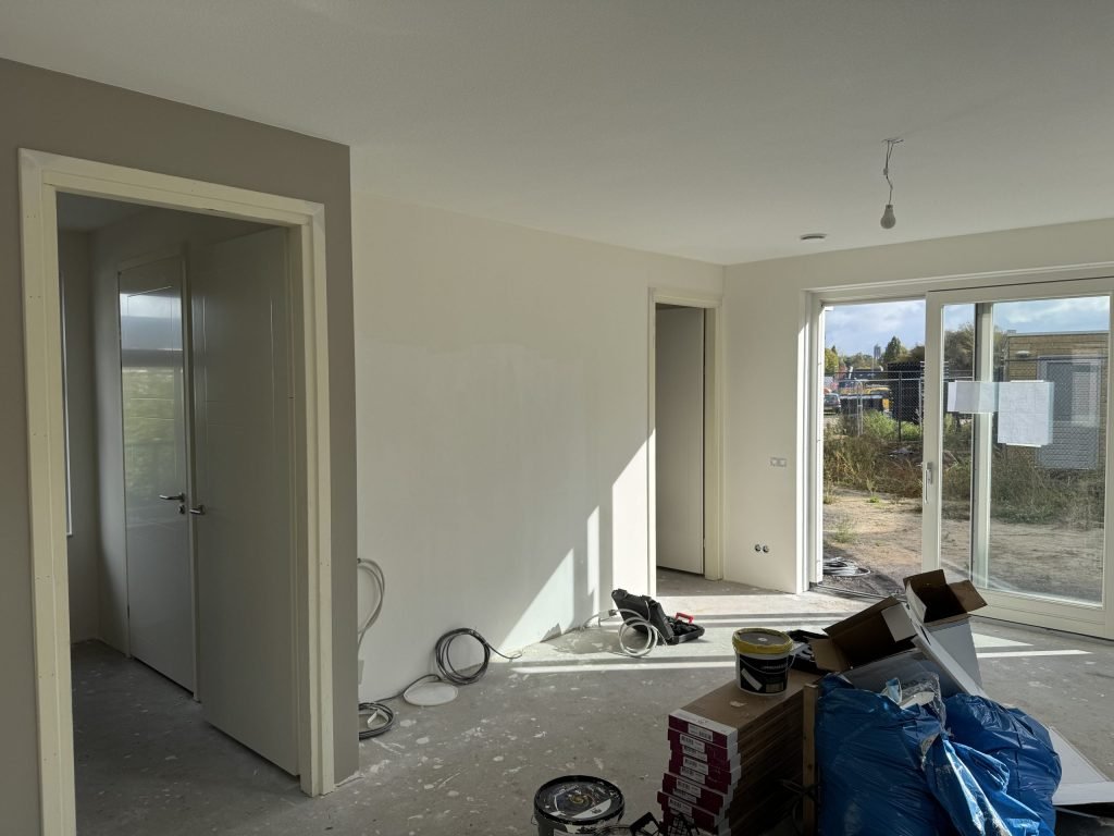 Nieuwe woning tijdens de afwerking, met verfemmers en dozen op de betonvloer bij de tuindeuren