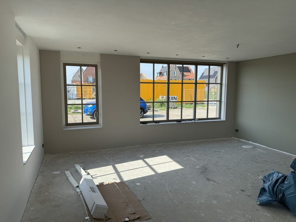 Kamer in een nieuwbouwhuis met roedenramen en wanden in een warme grijsgroene tint